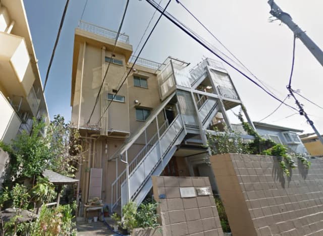 - 鉄骨で造られた三階建てのアパート、周囲に緑があり、階段と手すりがある外観の写真