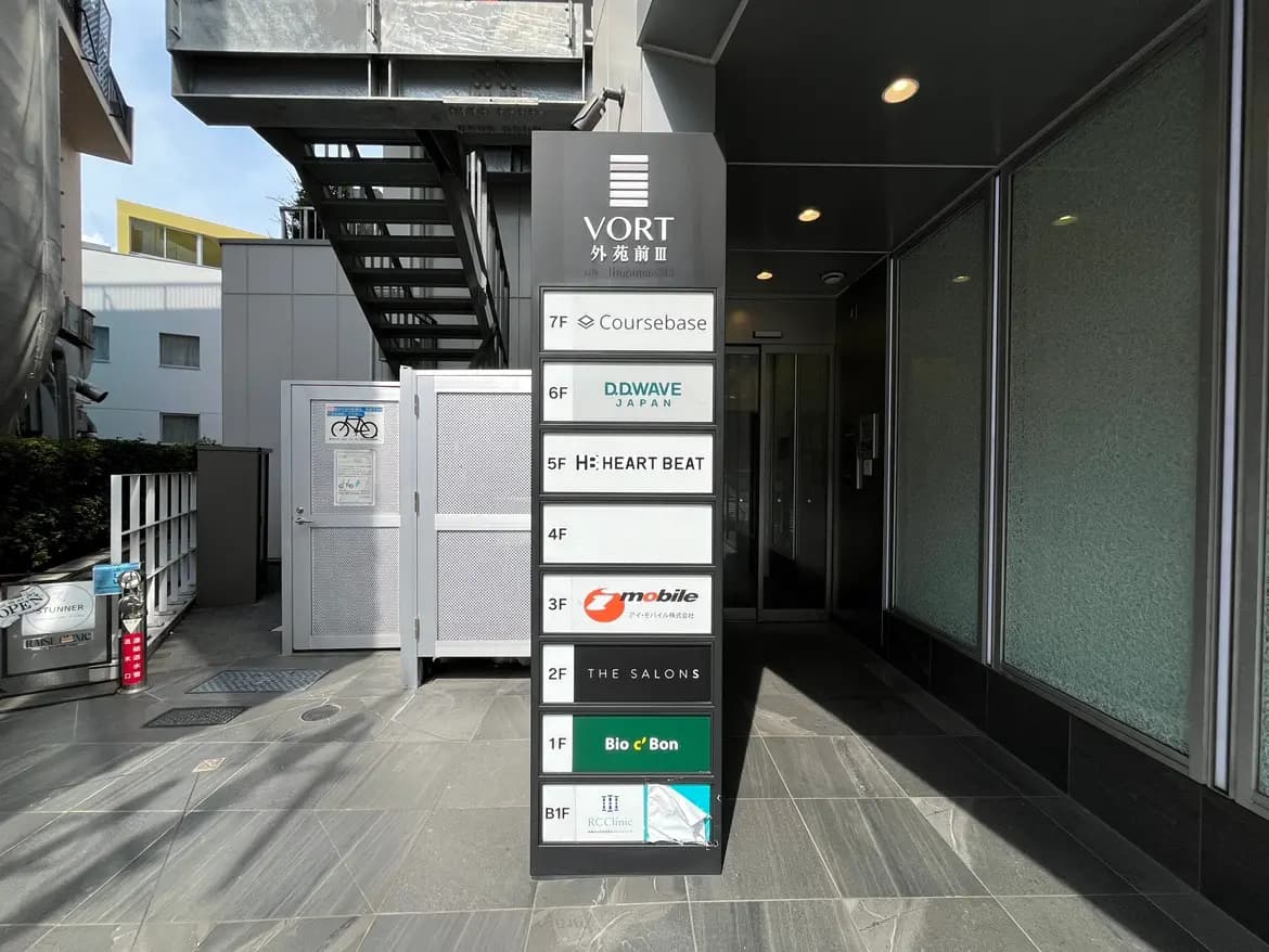 - 建物の入口に設置された店舗案内サイン、各階のテナント名が表示されたモダンなデザインの看板