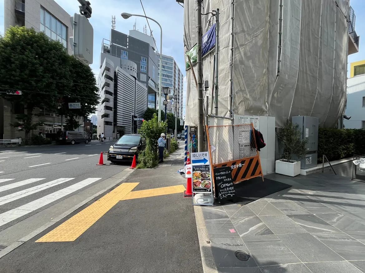 - 都会的な風景、工事中のビル、街角にある飲食店の看板と道路の標識、青空の下の様子