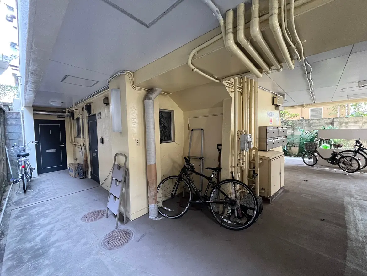 - 自転車が停められた狭い通路、壁に沿った配管と郵便受けのあるアパートのエントランス