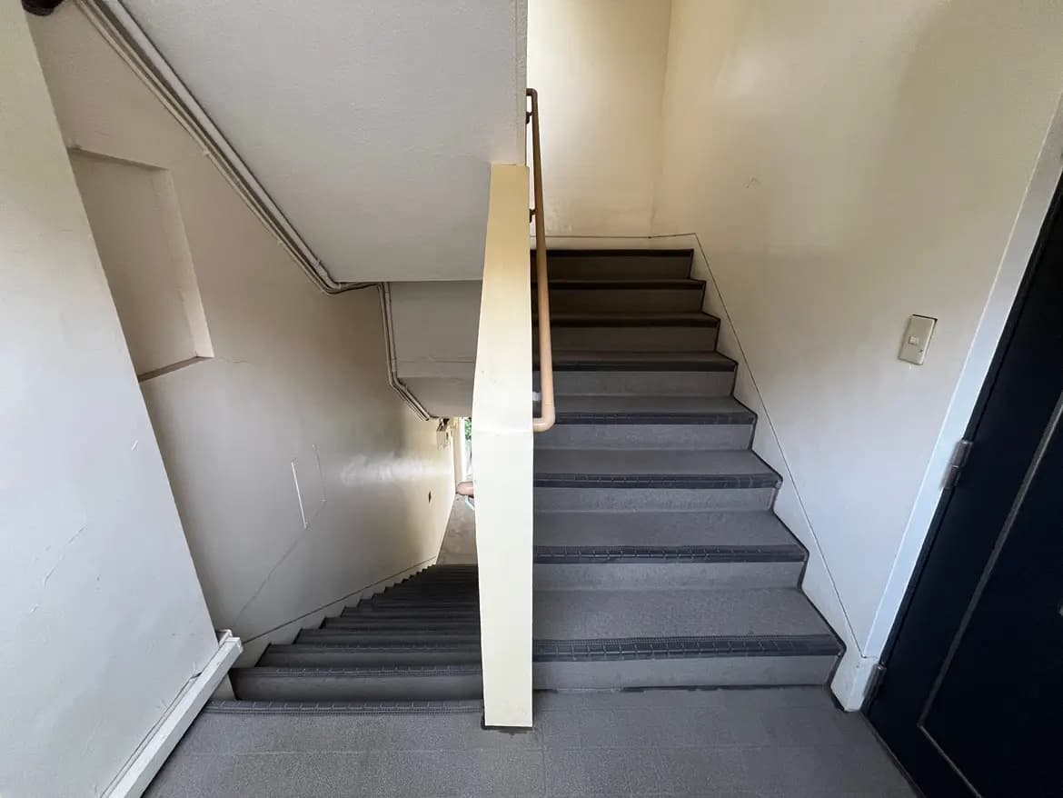 - 明るい色の壁と手すりがある階段、シンプルで安全なデザインの室内通路が見える