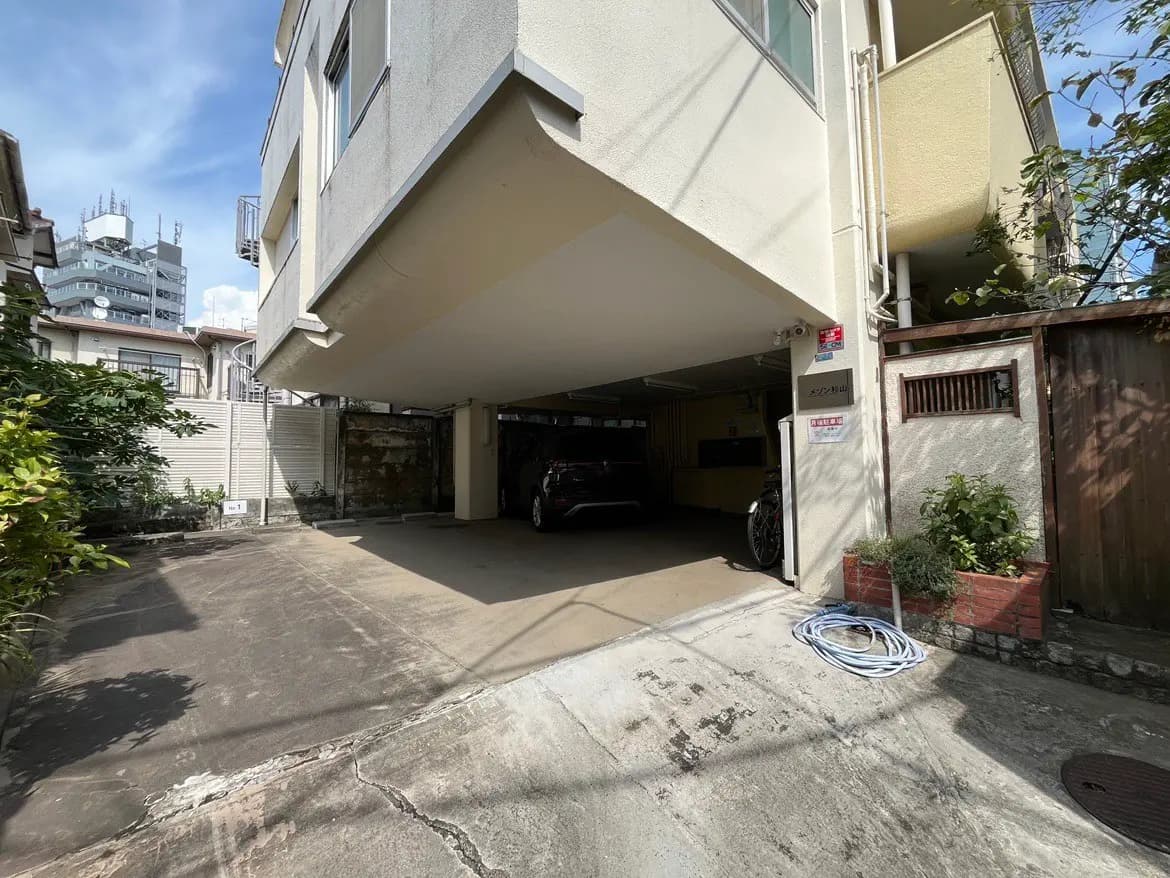 - 日当たりの良い車庫、上部に建物がある駐車スペースと周囲の緑が見える風景