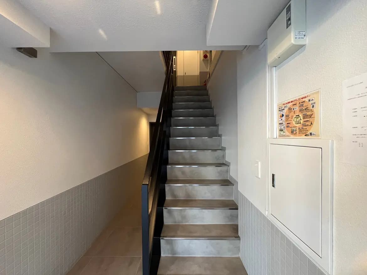 - 明るい照明が照らす清潔感のある階段、モダンなデザインの壁とフロアタイルが施されたエントランスエリア