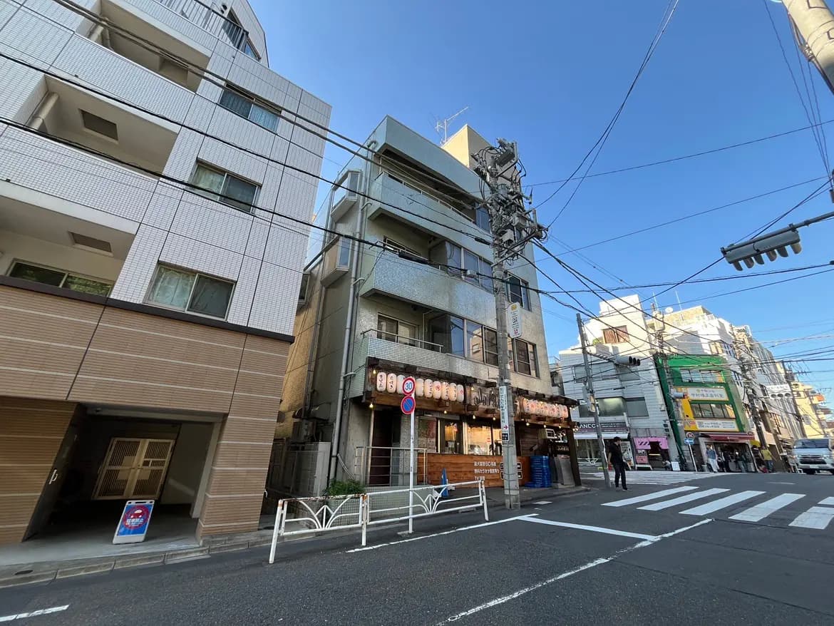 - 都市の通りに面した飲食店とアパートのビル、青空と電線が交錯する風景