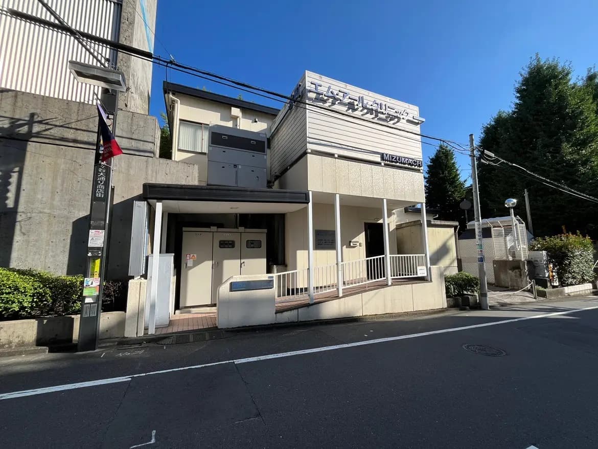 - 駐輪場と玄関のある白い外観の建物、青空の下で撮影された都市風景