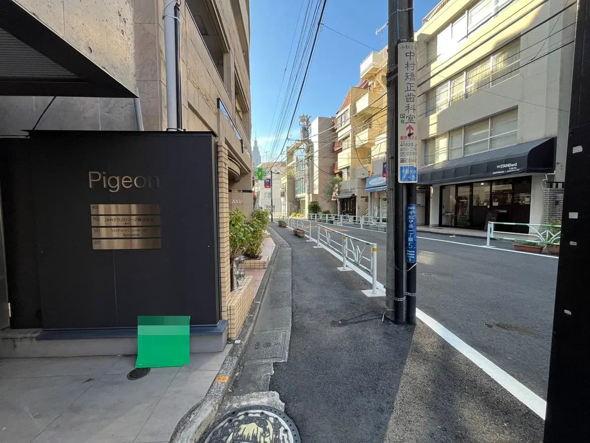 - 「Pigeon」と書かれた看板の前にあるビルの入り口、周囲に広がる街並みと清潔な歩道の風景