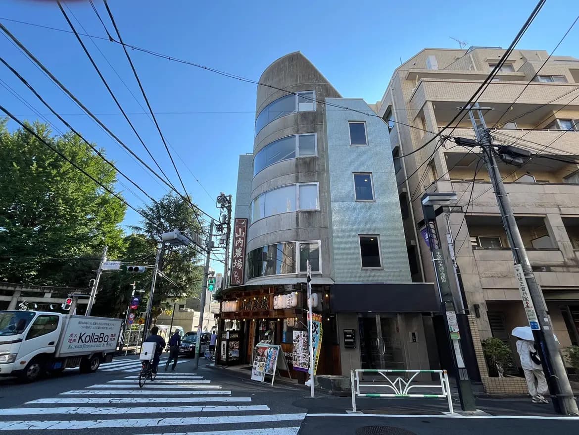 - 都会的な風景に立つモダンな建物、交差点には交通信号と人々、街の活気が感じられるシーン