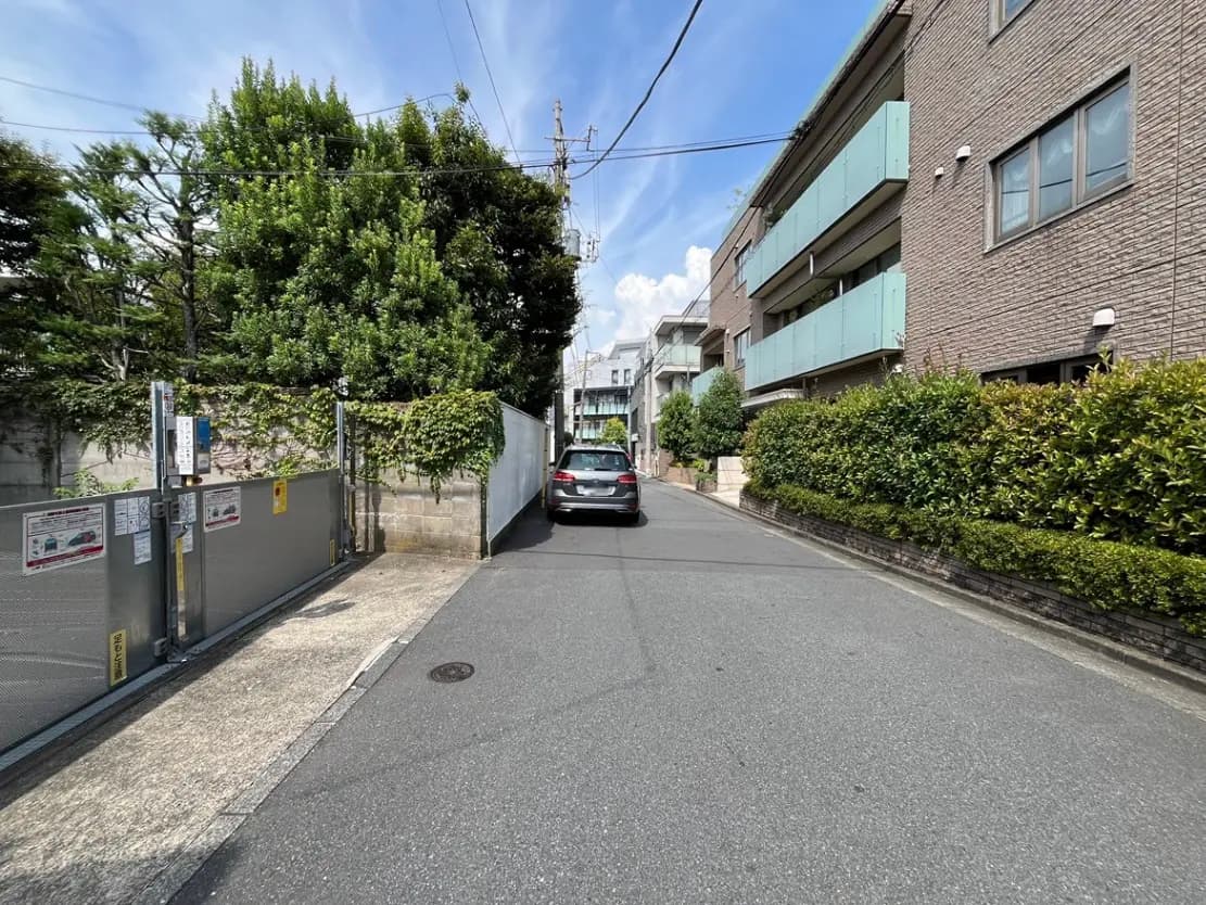 - 緑豊かな通りに面した住宅街、整備された歩道と並木、青空が広がる夏の風景