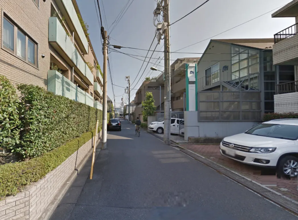 - 緑に囲まれた住宅街の風景、自転車に乗る人物と道路沿いのアパート、晴れた青空の下の景色
