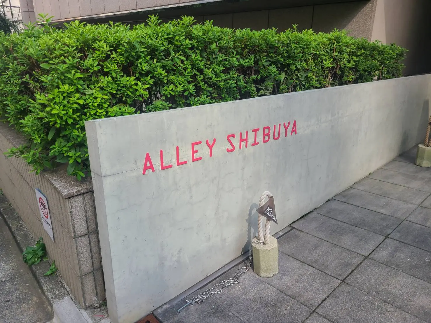 - 渋谷の小道を示す「ALLEY SHIBUYA」と書かれたコンクリートの看板と周囲の緑の植栽