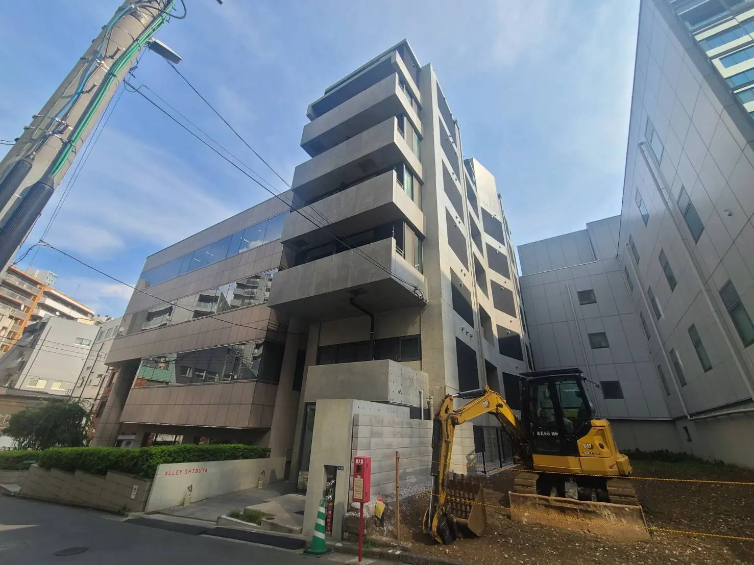 - 渋谷の新築ビル、モダンなデザインの外観と周囲の工事用機械、明るい青空が広がる街並み