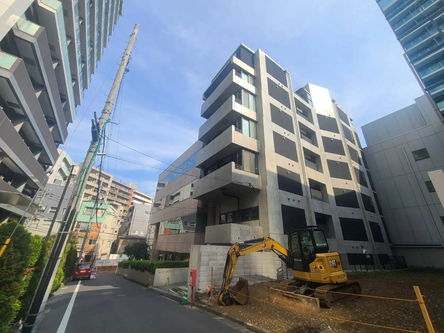 - 新しいビルの建設現場、隣接する高層ビルと建機が見える都市の風景、青空が広がるシーン