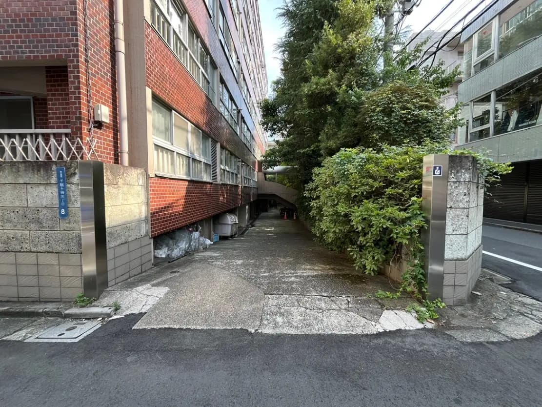 - 繁華街近くの住宅街に位置する、赤レンガの外壁を持つコンクリートビルと緑豊かな植栽の入り口、清掃作業が行われている様子が見える街路