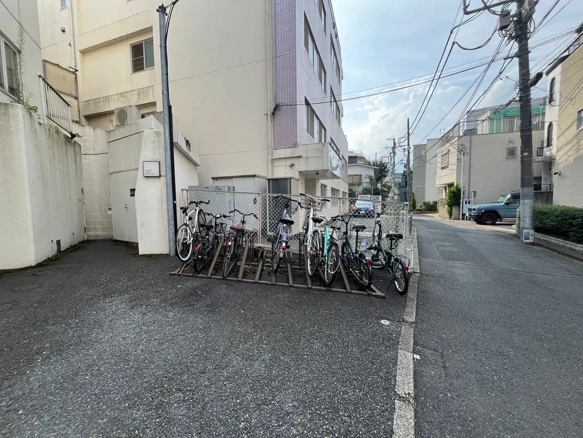 - 自転車が並んで停められた駐輪場、周囲に建物と電柱が立ち並ぶ都市の風景
