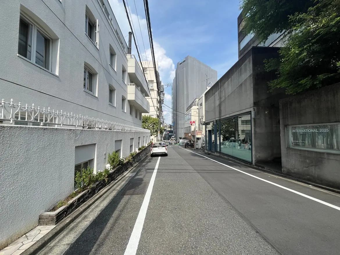 - 都市の静かな通り、白い建物が並ぶ片側の歩道、青空とビルが見える風景