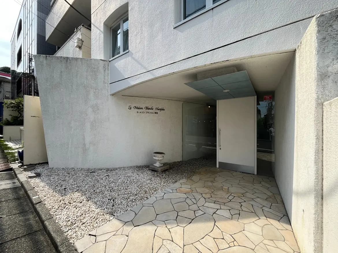 - モダンなデザインの建物のエントランス、白い壁と石の舗装、シンプルなデザインの看板と引き戸がある入り口の風景