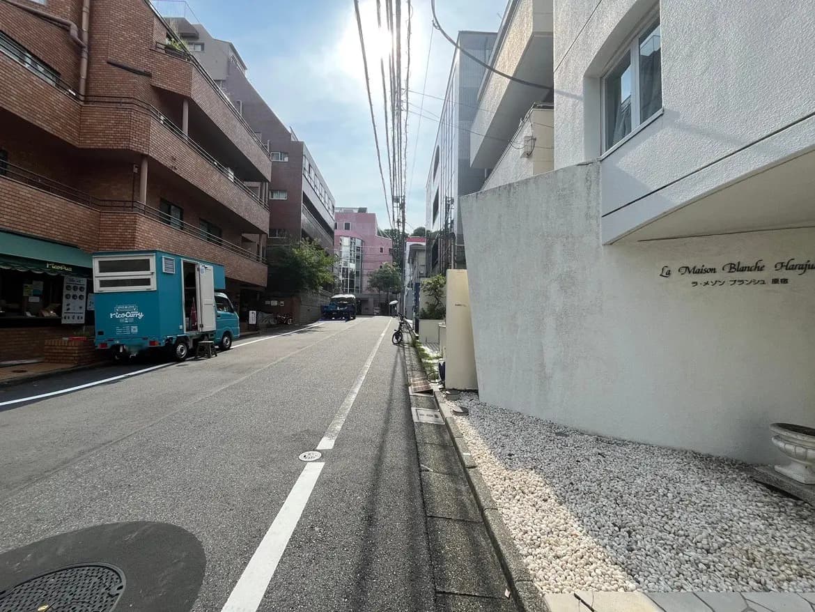 - 街の風景、アパートメントビルと白い壁の建物、青いトラックが停車している通りのシーン