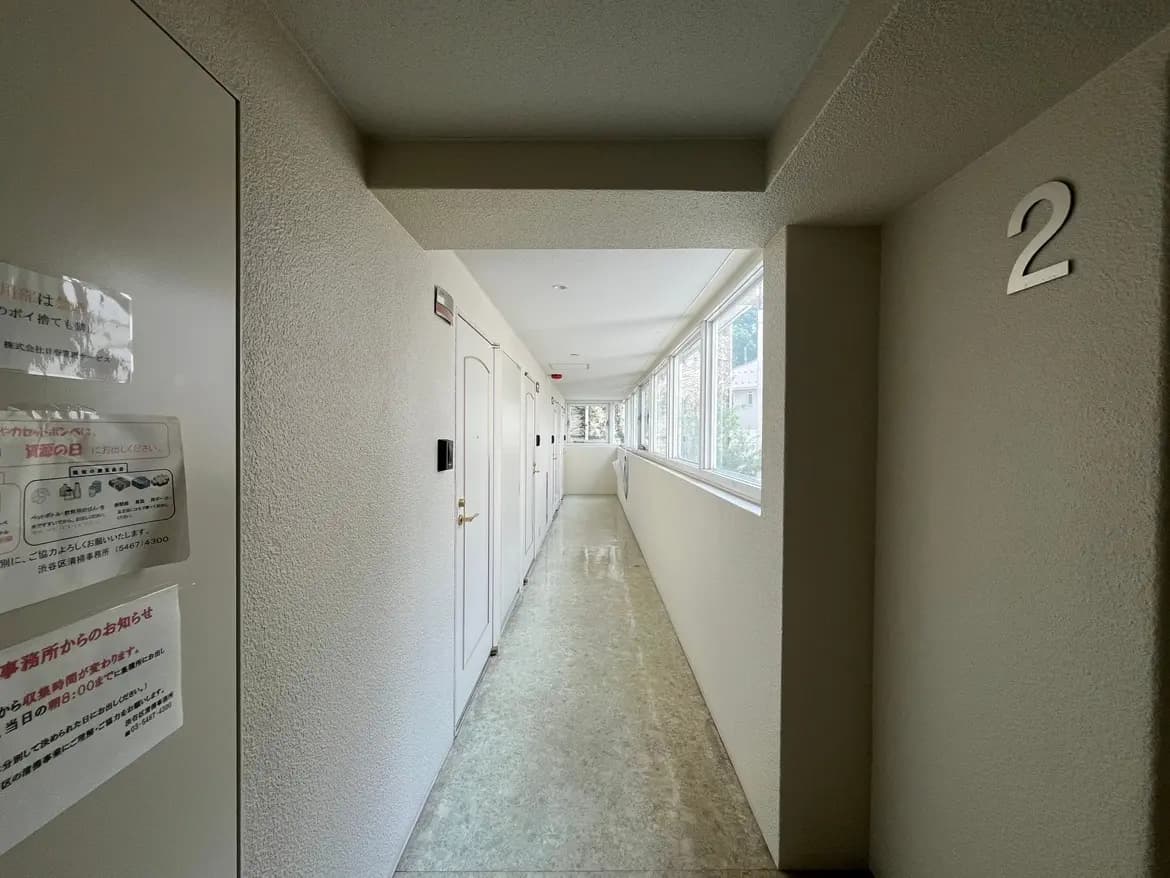 - 明るい廊下の風景、2号室の表示があり、窓から自然光が差し込む内装、整頓された扉が並ぶ様子