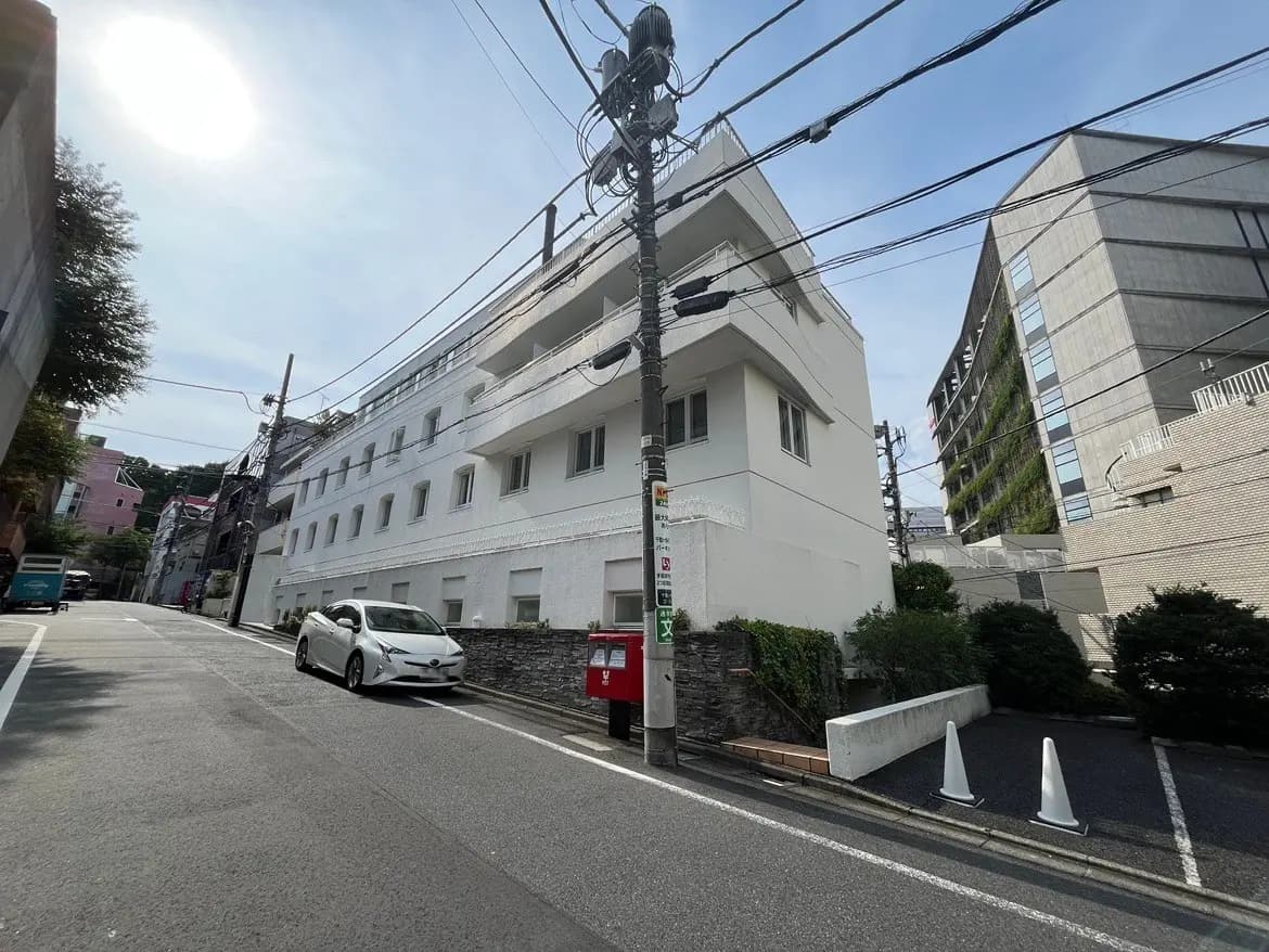 - 都市の風景にある白い外壁のマンション、近くに停められた車と電柱が並ぶ静かな街並みの写真