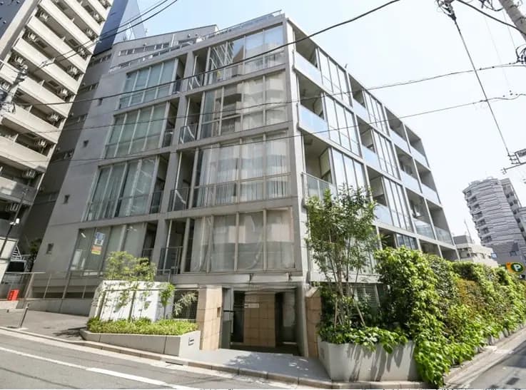 - 近代的なデザインのマンション外観、ガラスのバルコニーと緑豊かな植栽が特徴的な建物