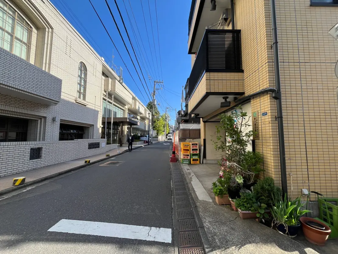 - 明るい青空の下、整然とした住宅街の風景、白いタイル張りの建物と植木が並ぶ歩道