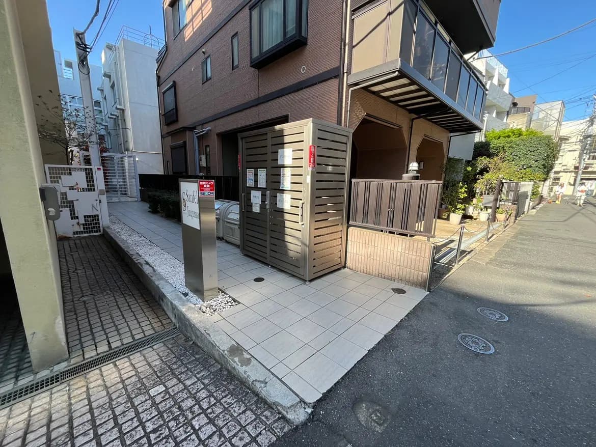 - 都市の住宅地にあるエントランス、敷石の通路と植栽、セキュリティボックスのあるアパートメントの外観