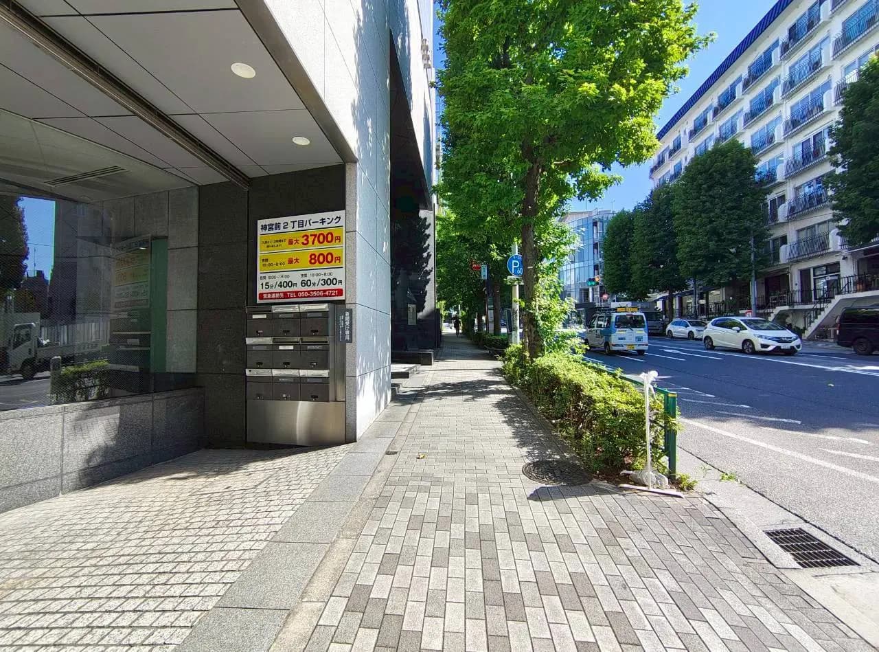 - 街路樹が整然と並ぶ歩道と建物の入り口、駐車料金が表示された看板があるシーン