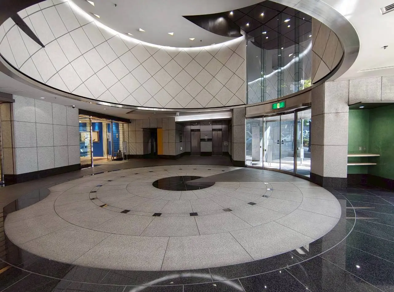- モダンなデザインのロビー、円形の石の床と照明が施された天井、エレベーターとガラスの入口があるインテリア