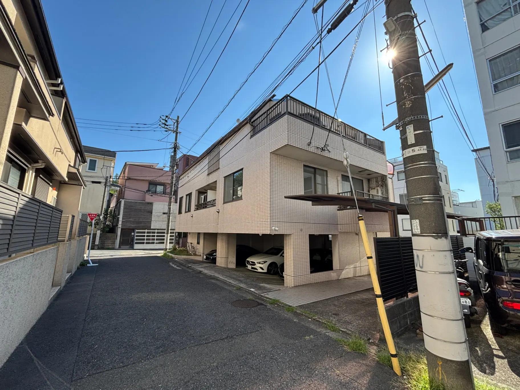 - 住宅街の眺望、青空の下に立つモダンな外観の建物、電柱と電線が交差する風景