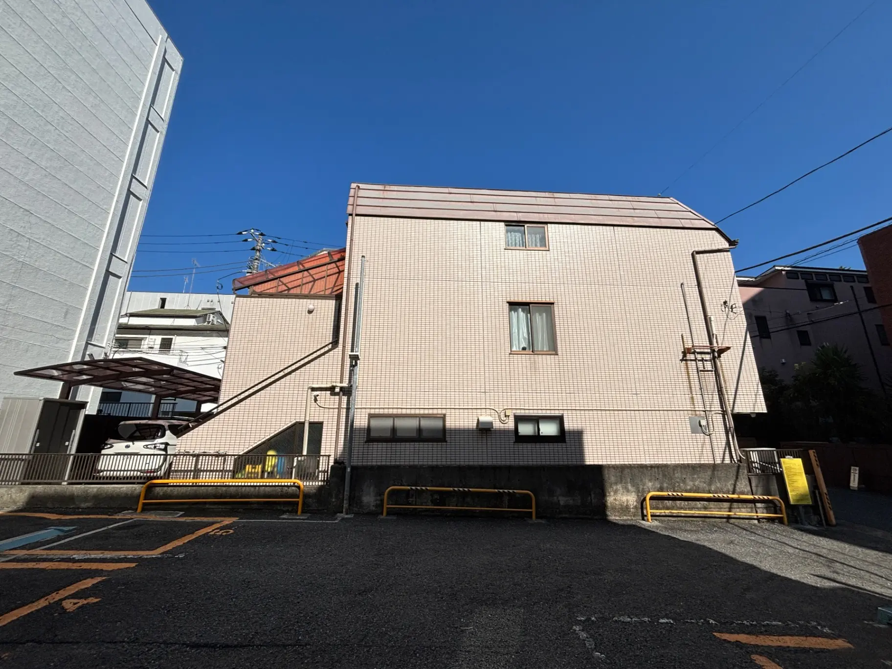 - 住宅街にある外観がピンクのタイルで覆われた2階建ての家、隣接するビルとの隙間に駐車スペースが見える景観