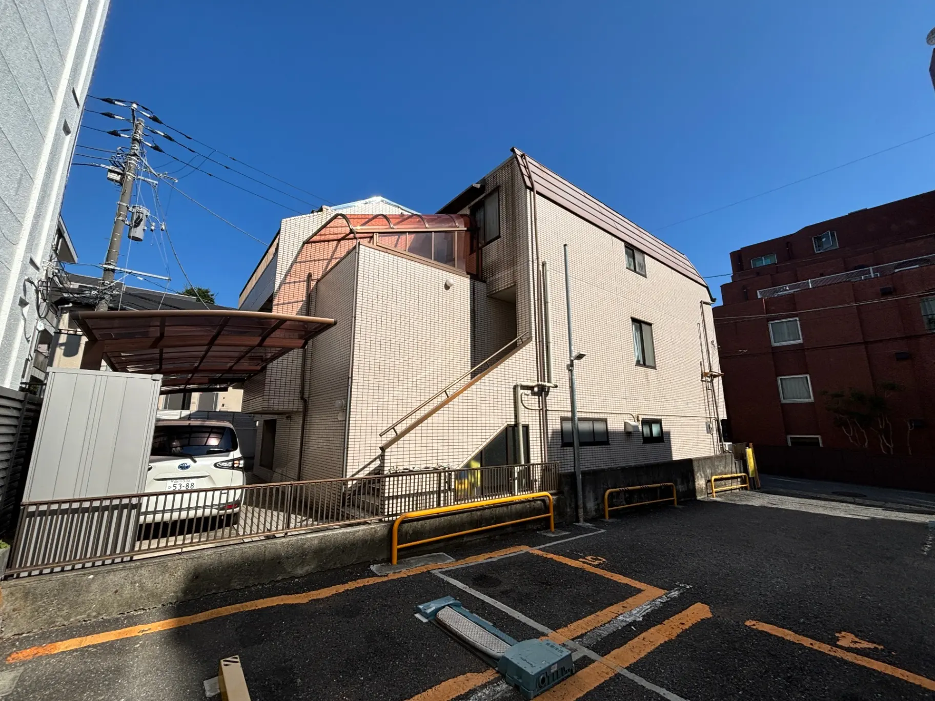 - 明るい青空を背景にした住宅街、駐車場に停められた白い車とレンガ造りの建物が並ぶ風景
