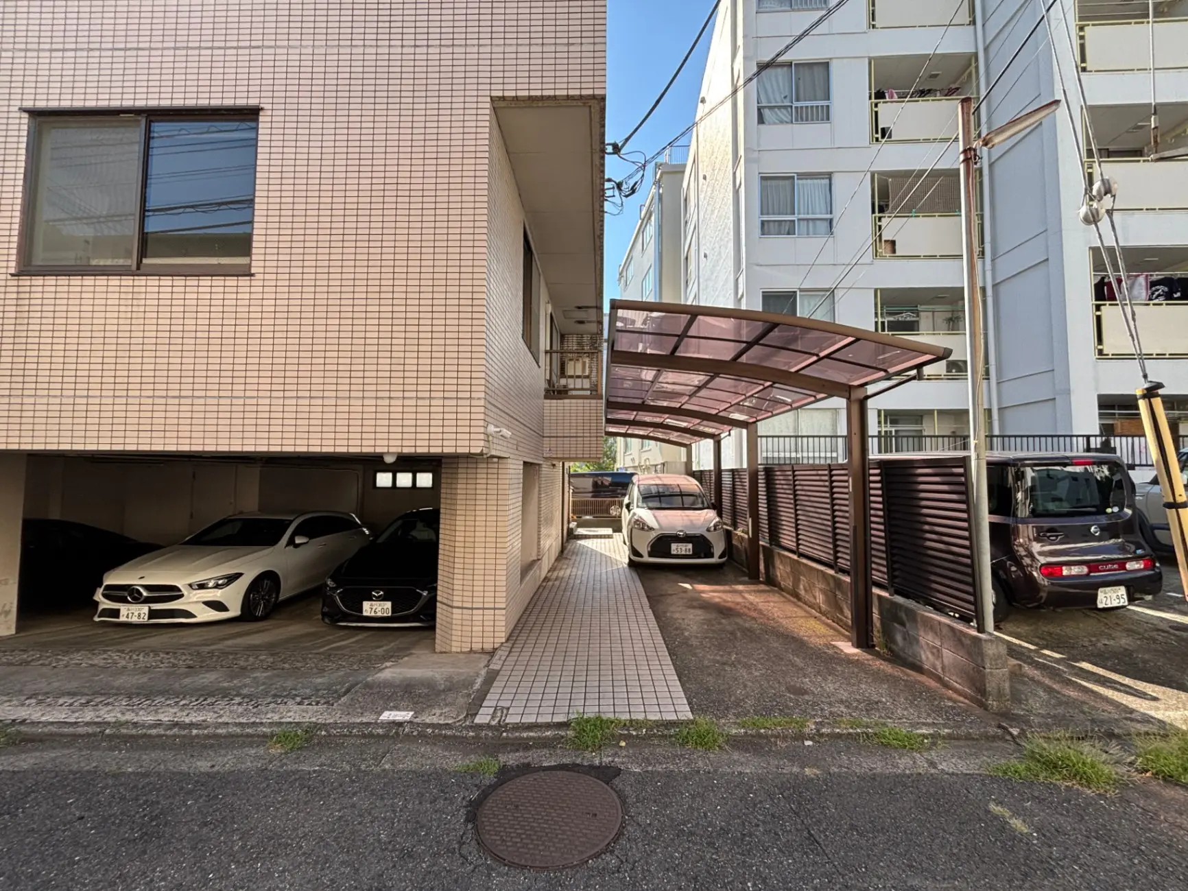 - 駐車場に並ぶ白と黒の車、アパートの外観と青空が広がる風景