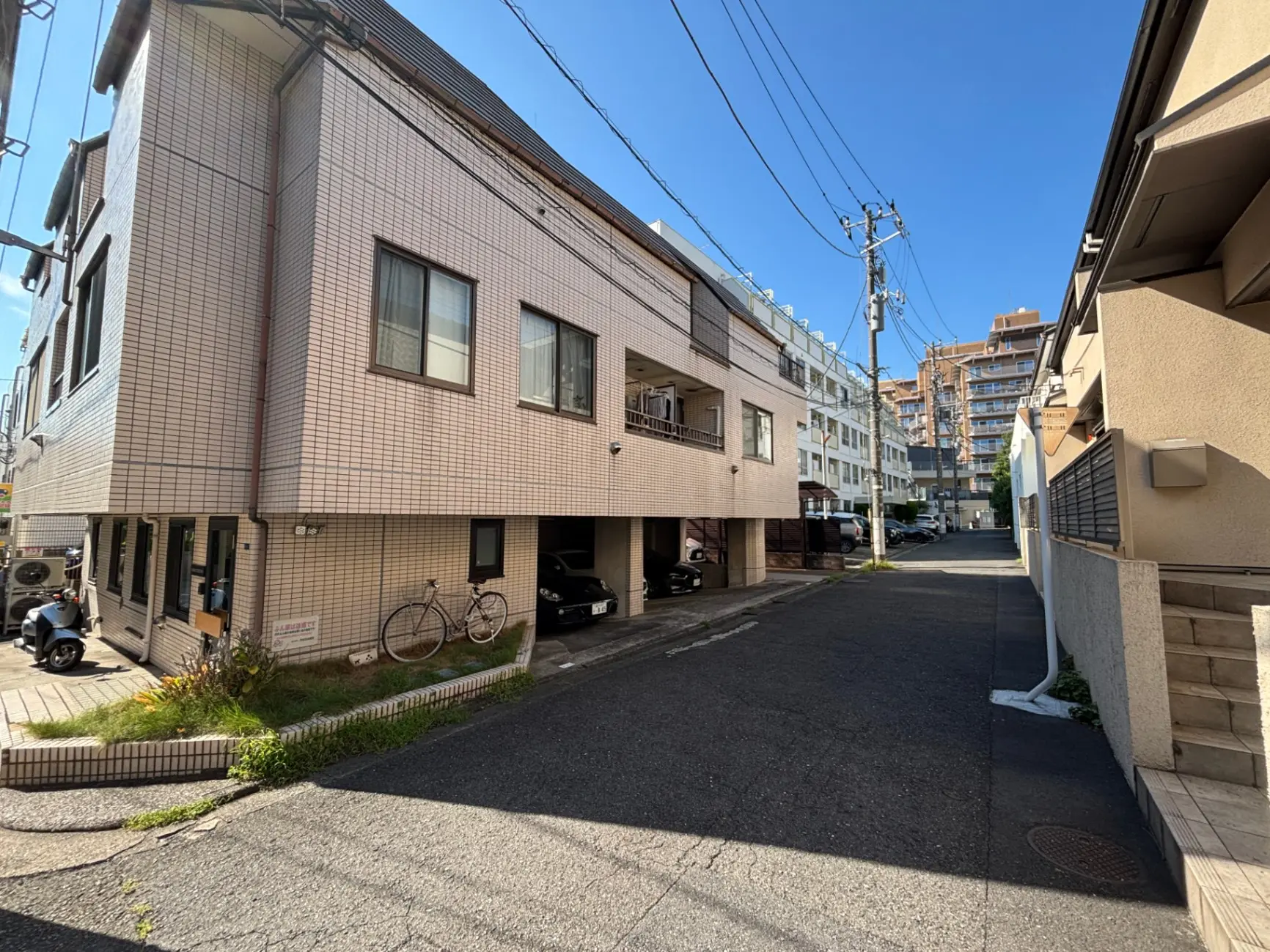 - 明るい青空の下、住宅街の道路とレンガ造りの建物、駐輪場に自転車が停まっている様子