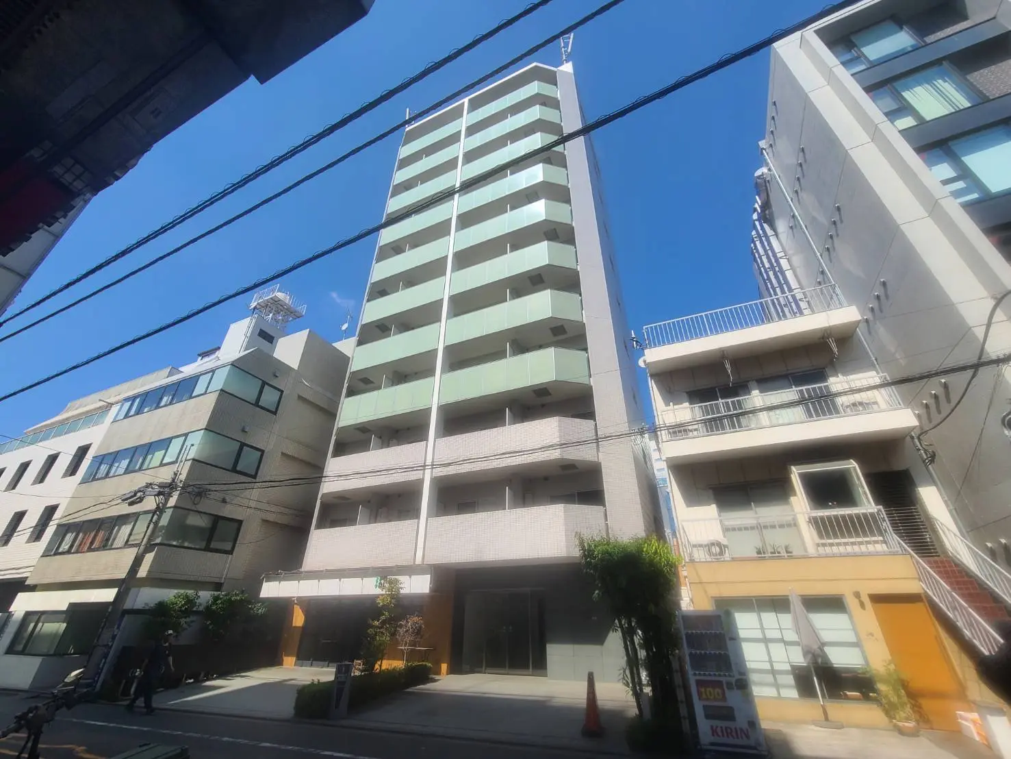 - 新しいデザインの高層ビル、周囲に低層の建物が立ち並び、青空が広がる都市の風景