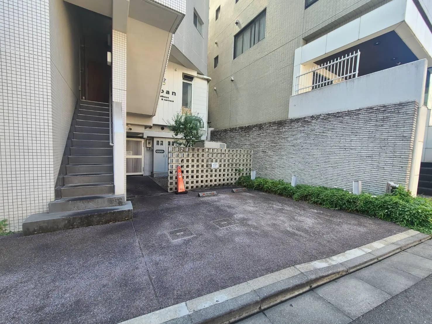 - 住宅ビルの入り口、階段、駐車スペースと壁面緑化のある外観、隣接する建物と舗装された道路