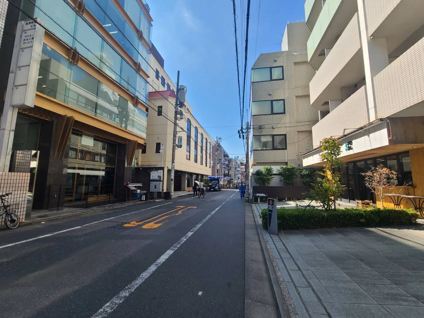 - 都会的なストリートシーン、ガラス張りのビルとタイル張りの建物、歩道には植栽が施された歩道とさまざまな店舗が並ぶ風景