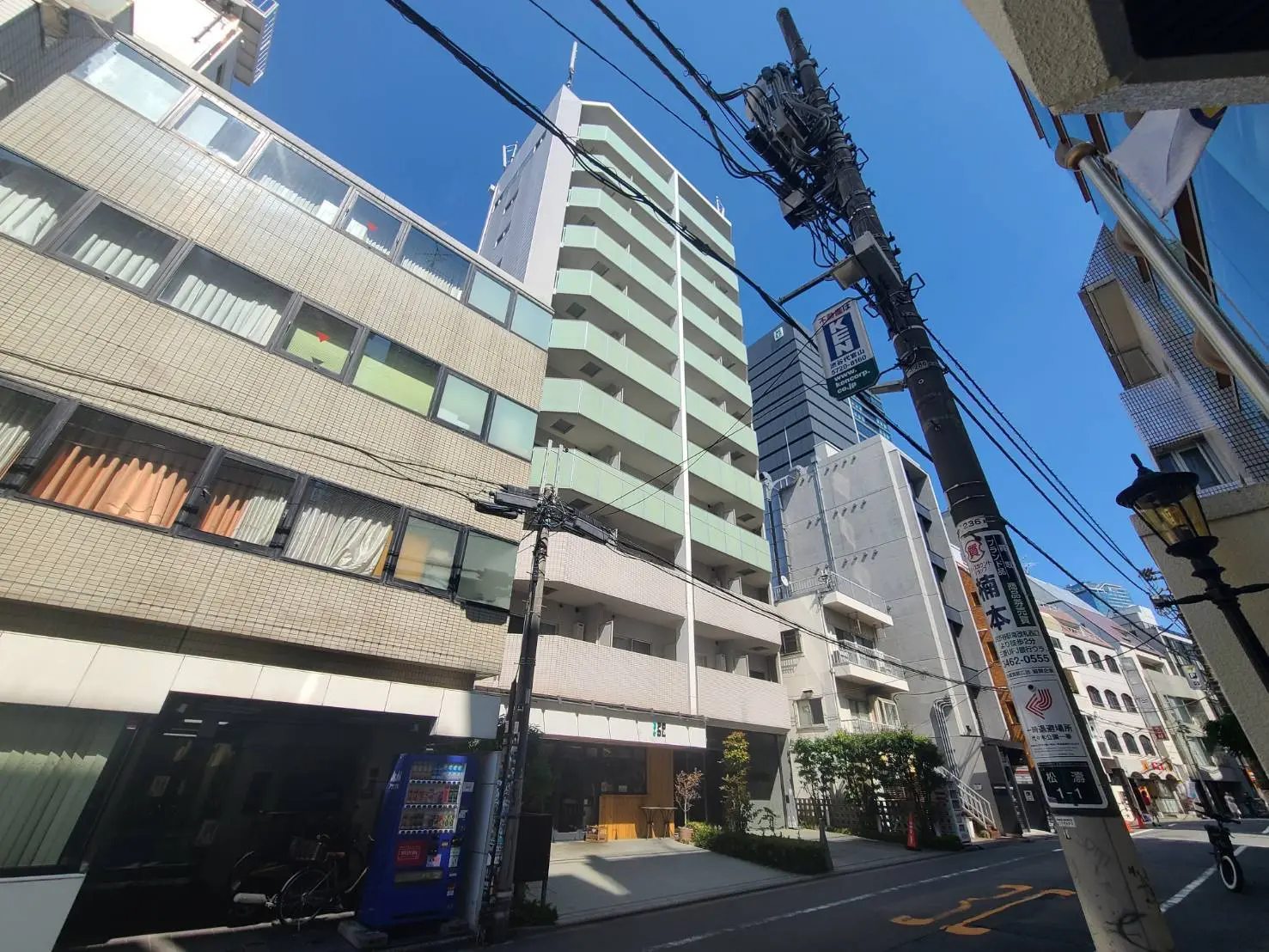 - 高層ビルのある都市の風景、街並みに沿ったビルと青空、電柱や看板が立ち並ぶ様子