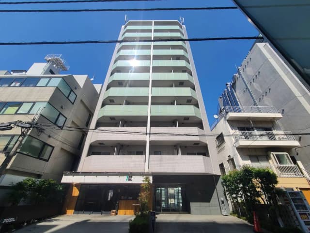 - 晴れた青空の下に建つ現代的なマンション、バルコニー付きで周囲に他の建物や電柱がある様子