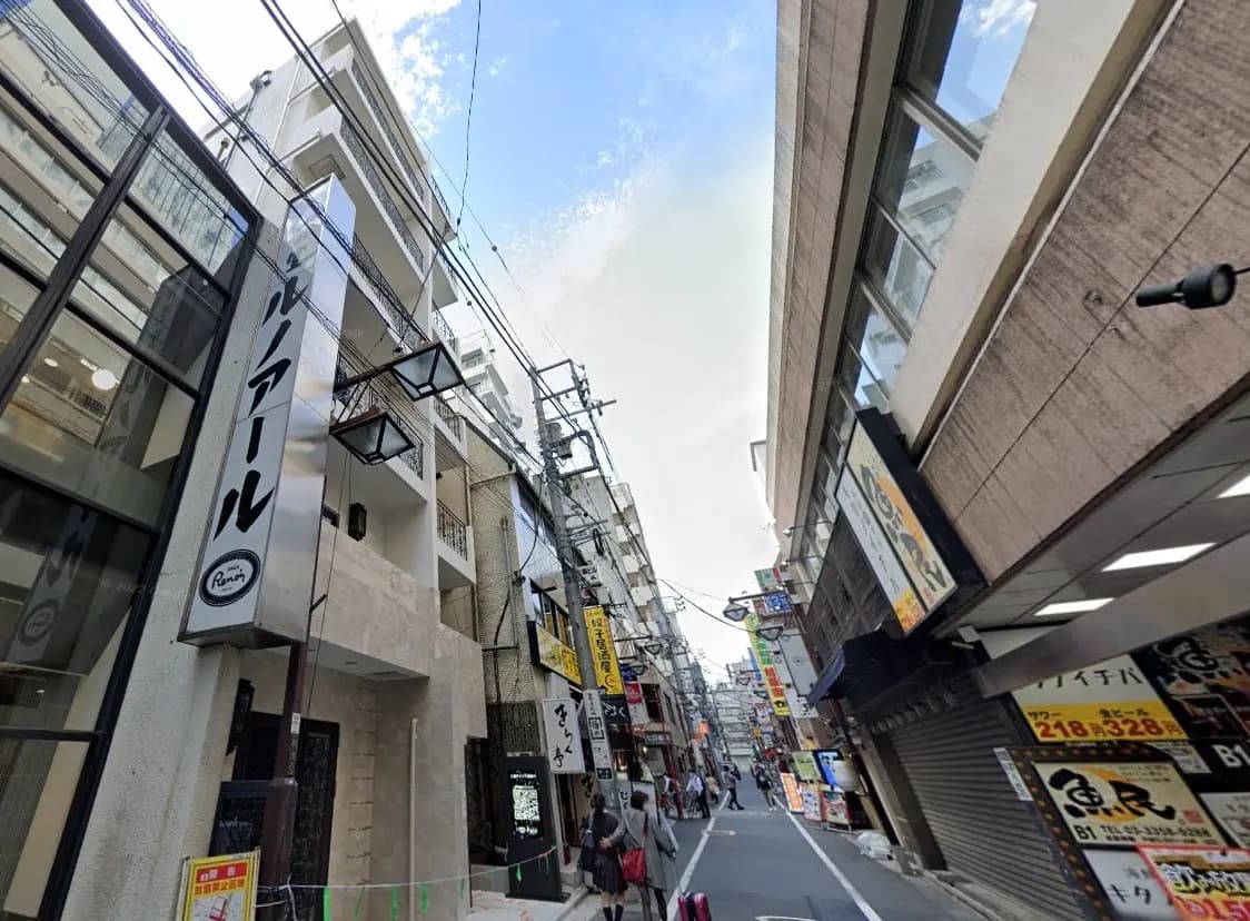 繁華街の細い通り、電線が交差し、様々な店舗の看板が並ぶシーン