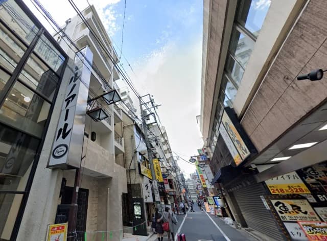 繁華街の細い通り、電線が交差し、様々な店舗の看板が並ぶシーン