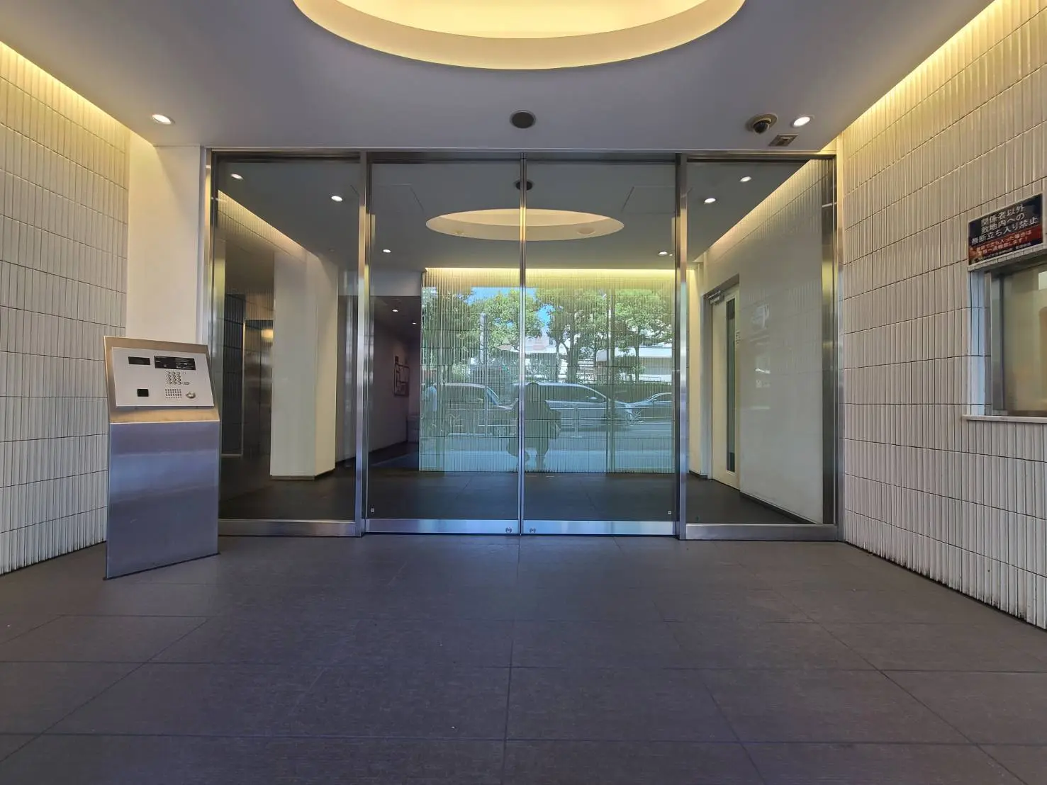 - モダンなビルのエントランス、ガラスドアと金属製インタフォン、明るい照明が特徴のロビーエリア