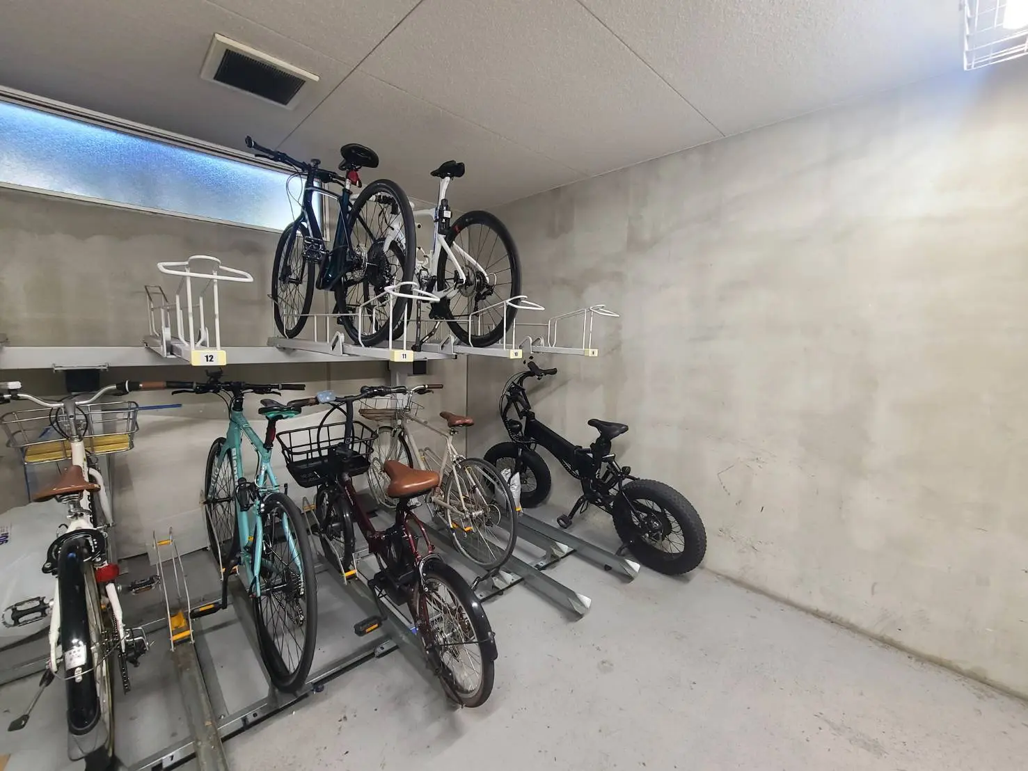 - 駐輪場の自転車置き場、複数の自転車が壁面のラックに整理されている様子、明るい照明が設置された室内の環境