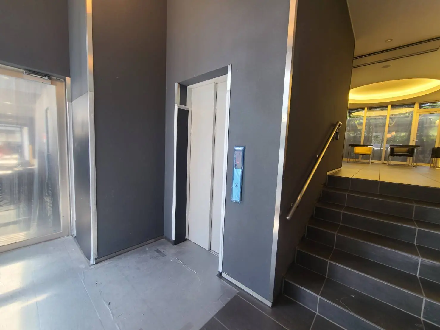 - モダンなエントランス、エレベーターと階段、落ち着いた色合いの壁と床材のインテリア