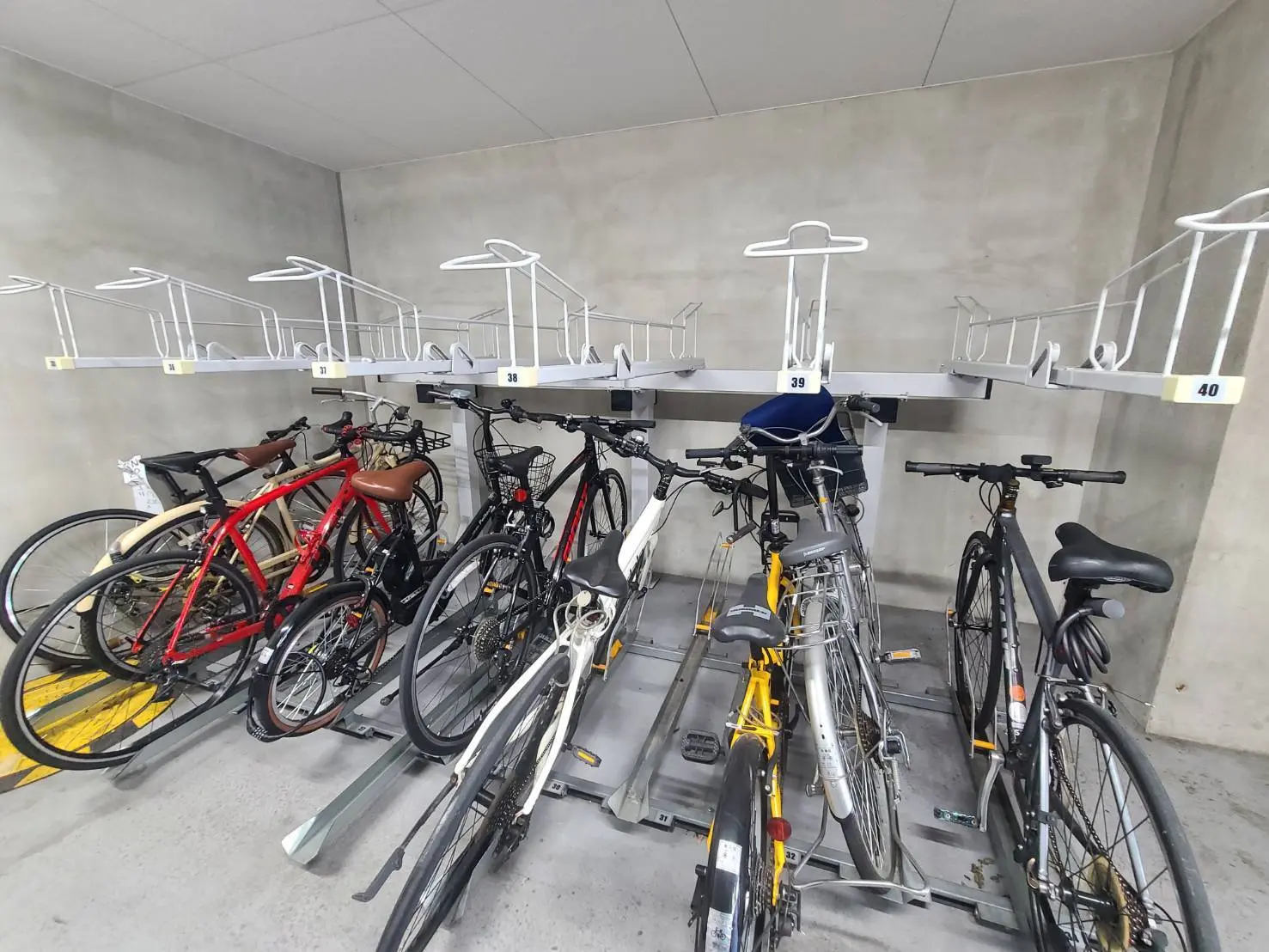 - 駐輪場の自転車ラックに停められた複数の自転車、周囲のコンクリート壁と清潔感のあるスペース