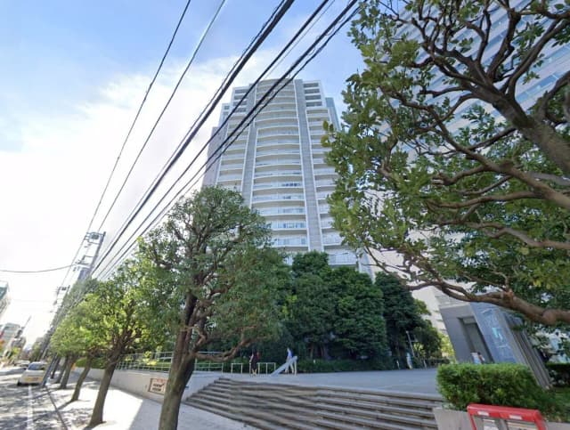 - 高層ビルの外観、周囲に並ぶ街路樹と電線、青空の下に立つ都市風景