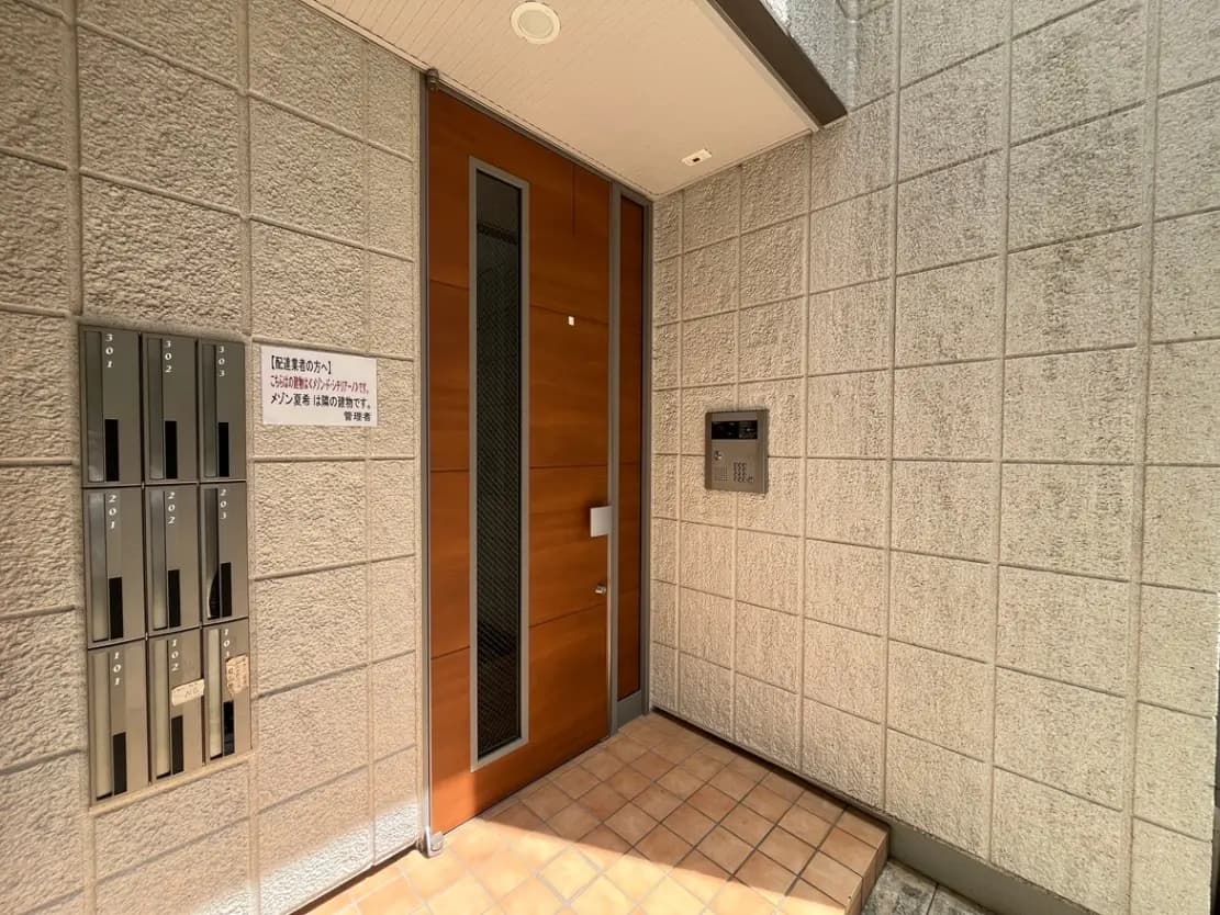 - モダンな建物のエントランス、木製の扉と呼び鈴、郵便受けが並ぶ洗練された外観