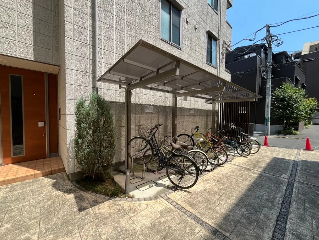 - 自転車置き場の屋根付きスペースに停められたさまざまな色の自転車、周囲には緑の植物と明るい青空が広がる景観