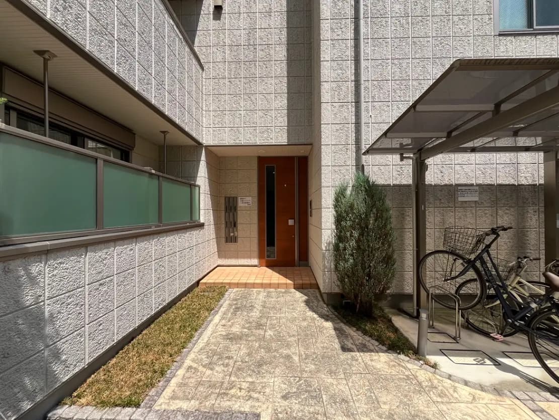 - 現代的なアパートのエントランス、シンプルなデザインの外観、敷石と整った植栽が施されたアプローチと自転車置き場
