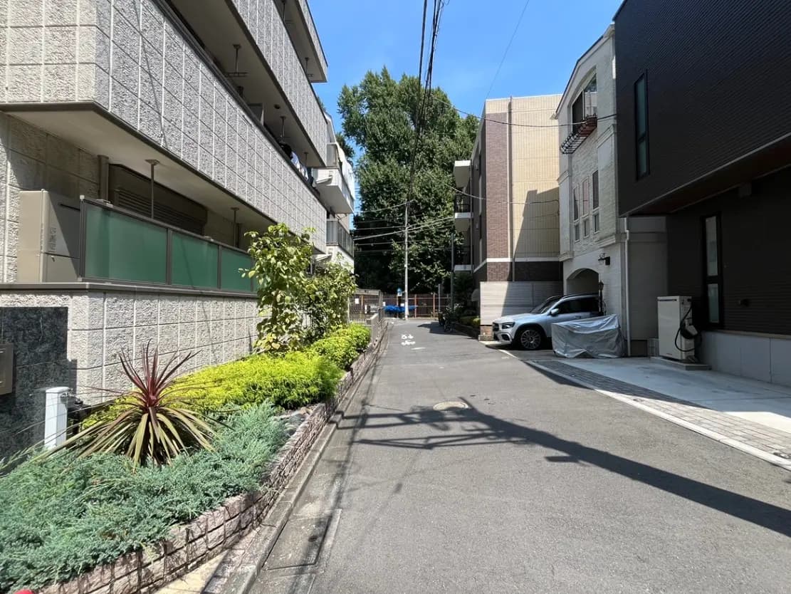- 緑豊かな植栽が施された住宅街の道路、小型車が停まっている住宅と青空が広がる風景
