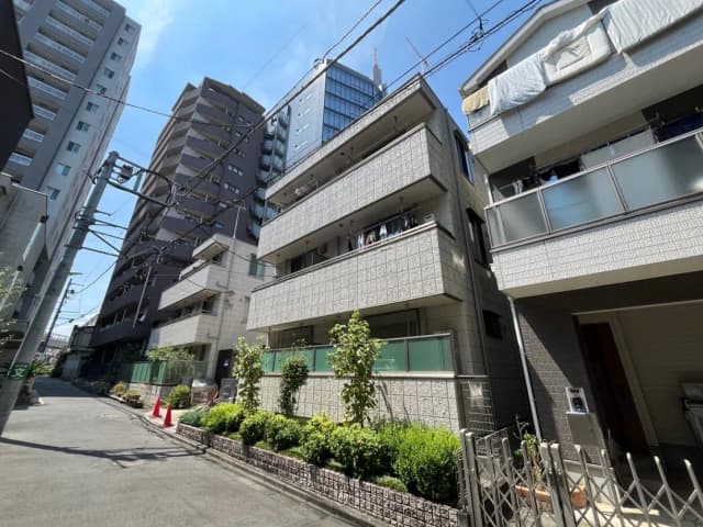 - 都市的な街並みに囲まれたモダンなアパートメント、植物が植えられた緑豊かな歩道と洗濯物が干されたバルコニーの景観